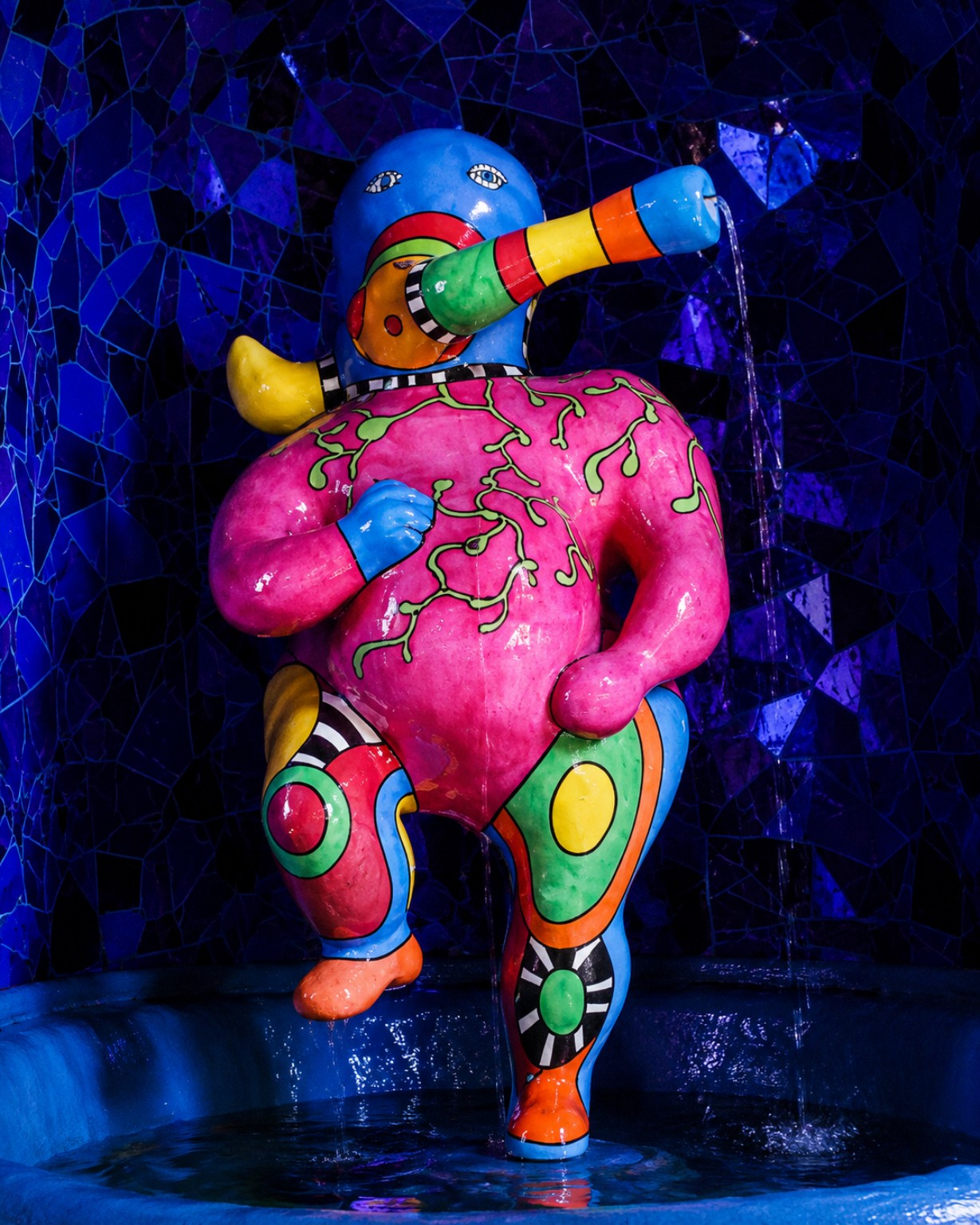Colourful sculptural figure against a deep blue mosaic